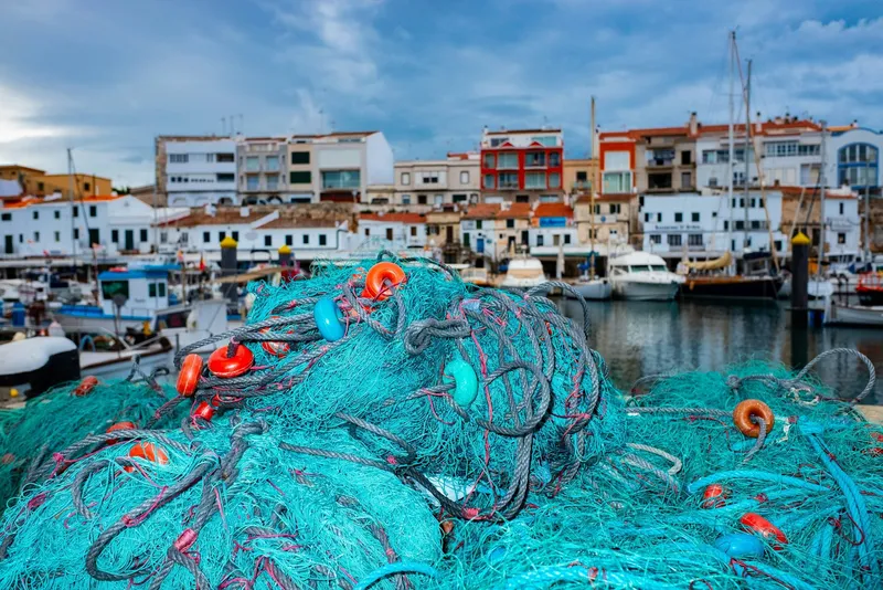 Redes de pesca turquesa en el puerto de Ciutadella con casas al fondo