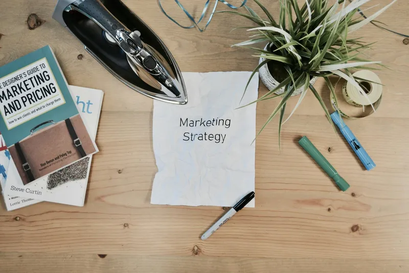 Mesa de trabajo con libros de marketing y un papel que dice Marketing Strategy